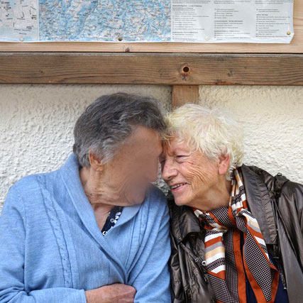 Zwei Seniorinnen sitzen vor einem Haus auf der Bank